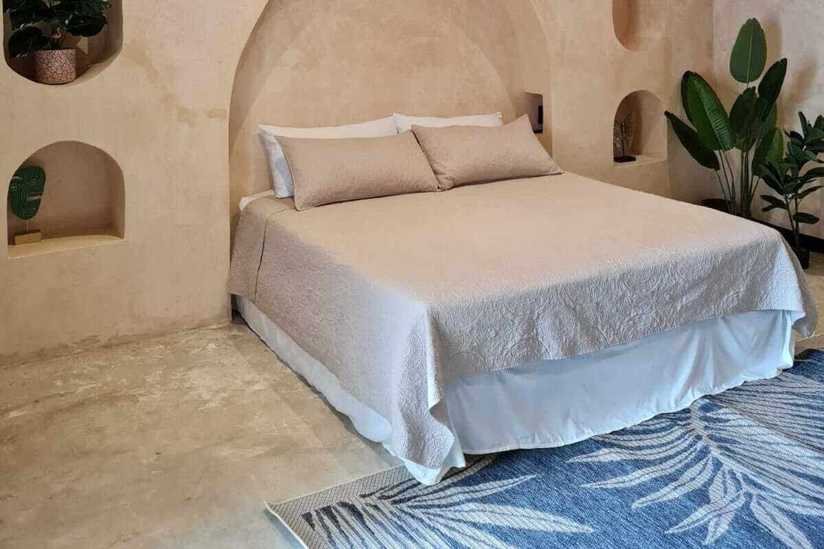 A bedroom with a large bed, built-in shelving with plants, and a patterned rug.