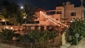 Un bâtiment doté d’une toiture en chaume, un bâtiment moderne avec une façade en pierre et des guirlandes lumineuses.