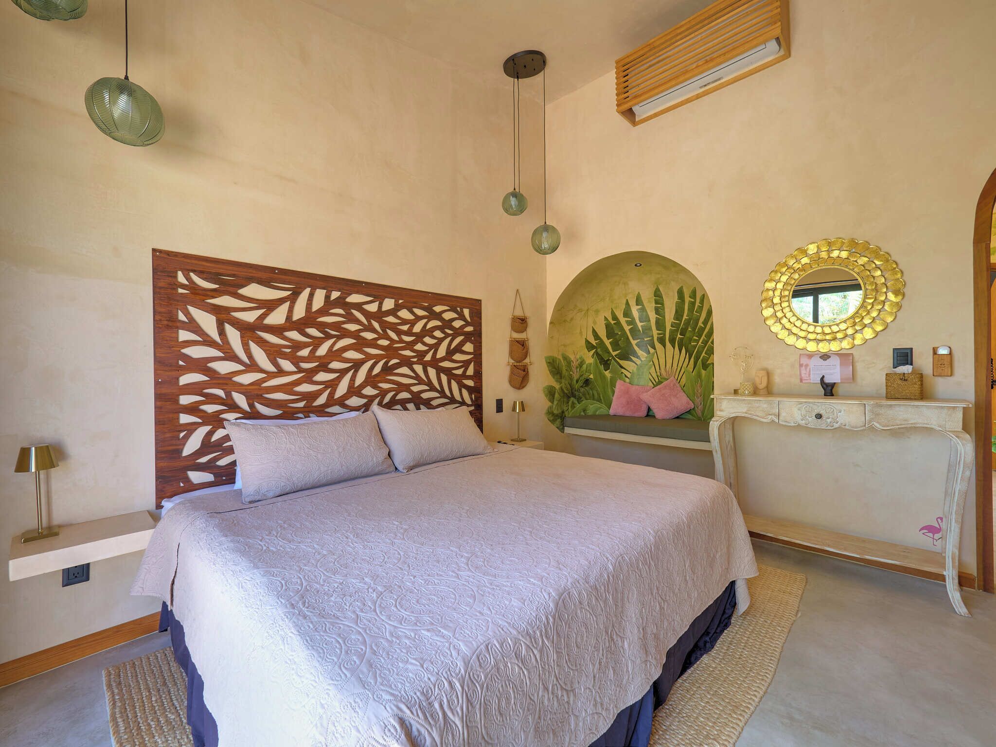 Une chambre à coucher comprenant un lit, une tête de lit en bois, une coiffeuse avec un miroir et un luminaire fixé au mur.