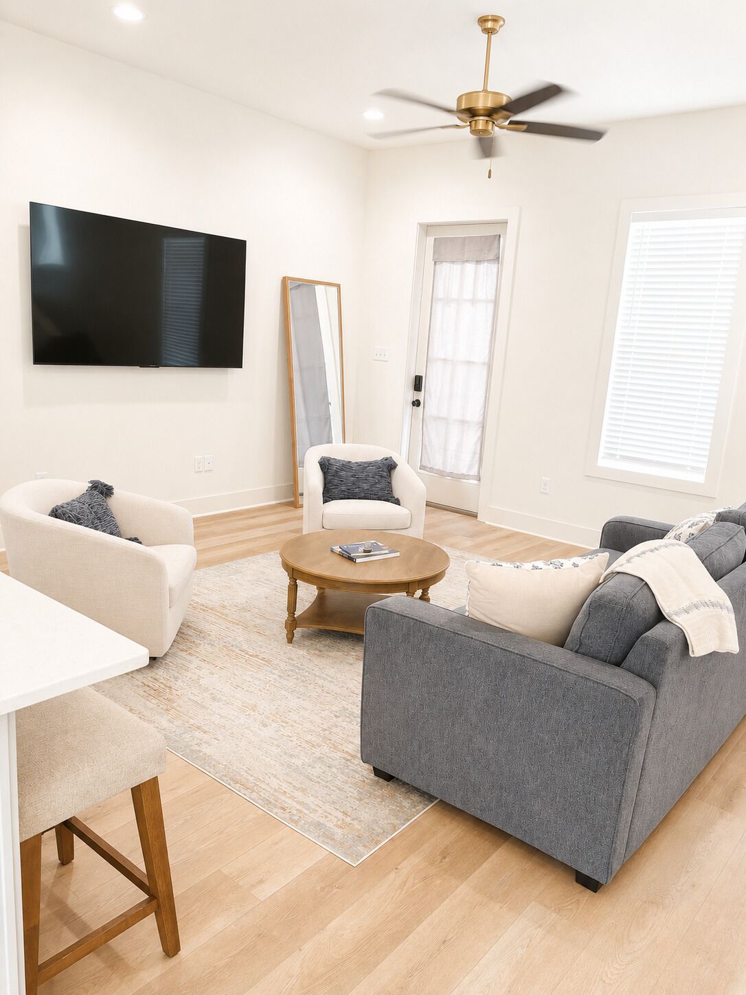 A modern living room with a flat-screen TV, a ceiling fan, a large mirror, and a grey sofa.