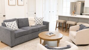 Ein modernes Wohnzimmer mit grauem Sofa, einem weißen Sessel, einem runden Couchtisch und einem Deckenventilator.
