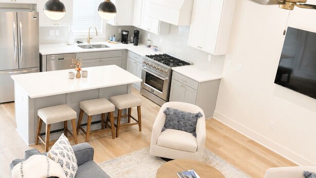 Eine moderne Küche mit weißen Schränken, einer zentralen Kochinsel und einem Essbereich mit grauem Sofa und Couchtisch.