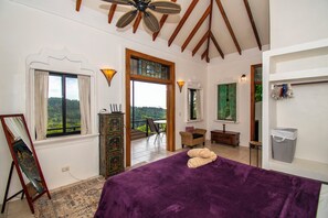 A bedroom with a large bed, a ceiling fan, a view through a window, and a balcony. - Stunning ocean and mountain views in Uvita! 1 bedroom house in the jungle (Uvita)