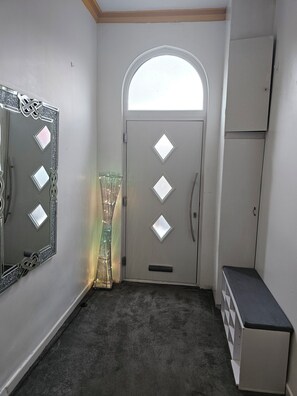 Um corredor com parede espelhada, porta com janelas em formato de losango, um banco e um armário.