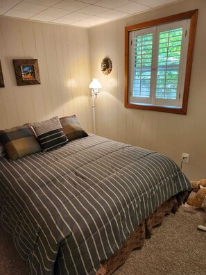 Un dormitorio con una cama, una lámpara, una ventana y un cuadro en la pared.
