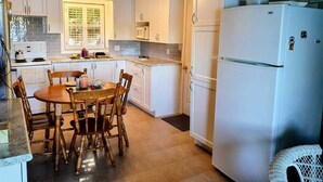 Eine kleine Küche mit weißen Schränken, einem Esstisch mit Stühlen, einem Kühlschrank und einer Mikrowelle.