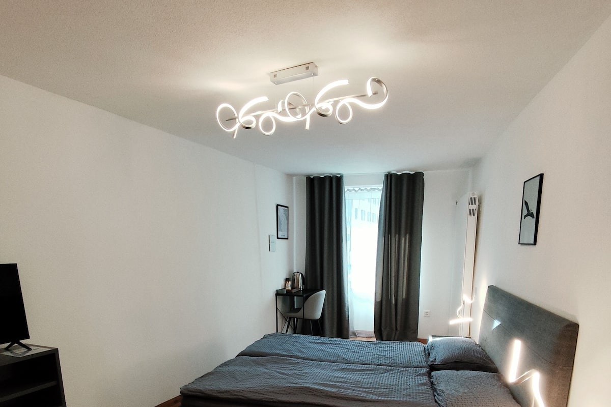 Un dormitorio moderno con cama, mesita de noche y escritorio con silla.