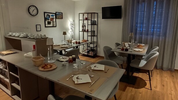 A modern dining area with a long table, chairs, a television, and a clock on the wall. - B&B Berninapass (Poschiavo)