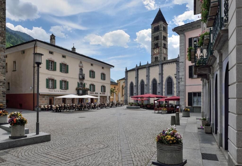 A courtyard with outdoor seating, a historic building with a clock tower, and a hotel with outdoor umbrellas.