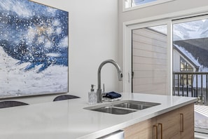 A modern kitchen with a large island, a double sink, and a view of a snowy landscape through the sliding glass doors. - 2BR Townhome with Mountain View 3min from DT Canmore (Canmore)