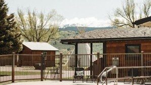 A swimming pool with a wooden deck, a fenced area, and a building with large windows. - Teton Valley RV Resort (Victor)