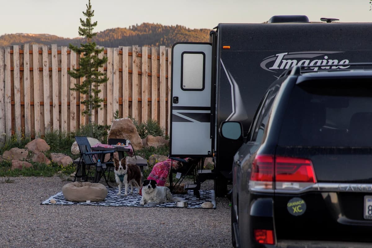 Montagem de camping com uma carreta, um carro e área para cães com manta e cama para cachorro.