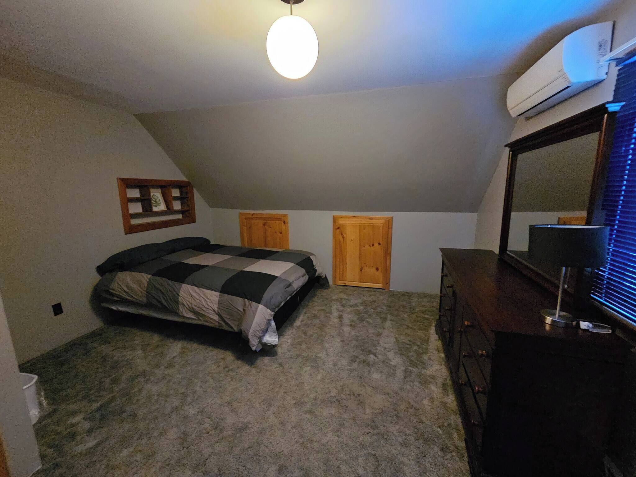 A bedroom with a bed, dresser, and an air conditioner on the wall.