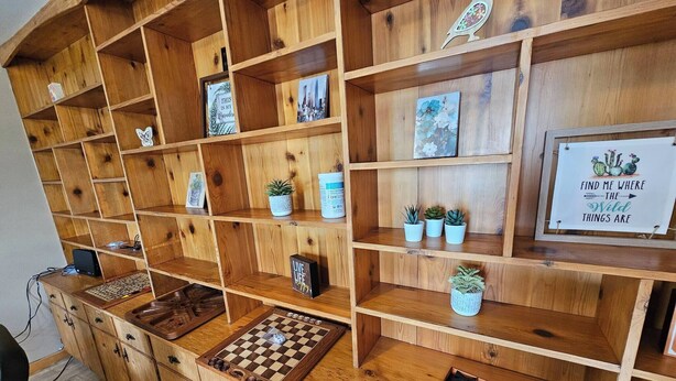 A wooden shelving unit with various items including a chessboard, potted plants, and decorative signs. - Bayview Hideaway is a 2 Story Home With Lots of Privacy (Whycocomagh)