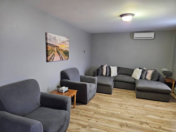 Un salon avec un canapé gris, une table basse en bois et un tableau accroché au mur.