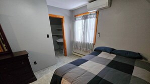 Ein Schlafzimmer mit Bett, Kommode, Kleiderschrank und einem Fenster mit Vorhängen.