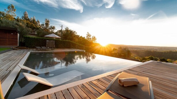 A serene outdoor swimming pool area with a wooden deck, lounge chairs, and a view of the landscape. - Golden View (Alvaiázere)