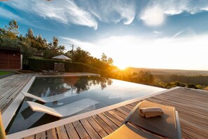 A serene outdoor swimming pool area with a wooden deck, lounge chairs, and a view of the landscape. - Golden View (Alvaiázere)