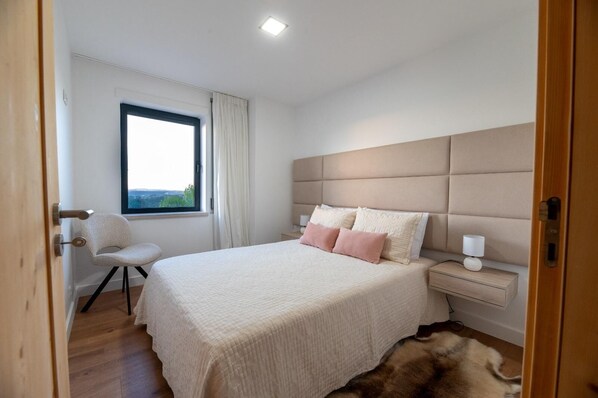 A bedroom with a bed, bedside table, chair, and a window.