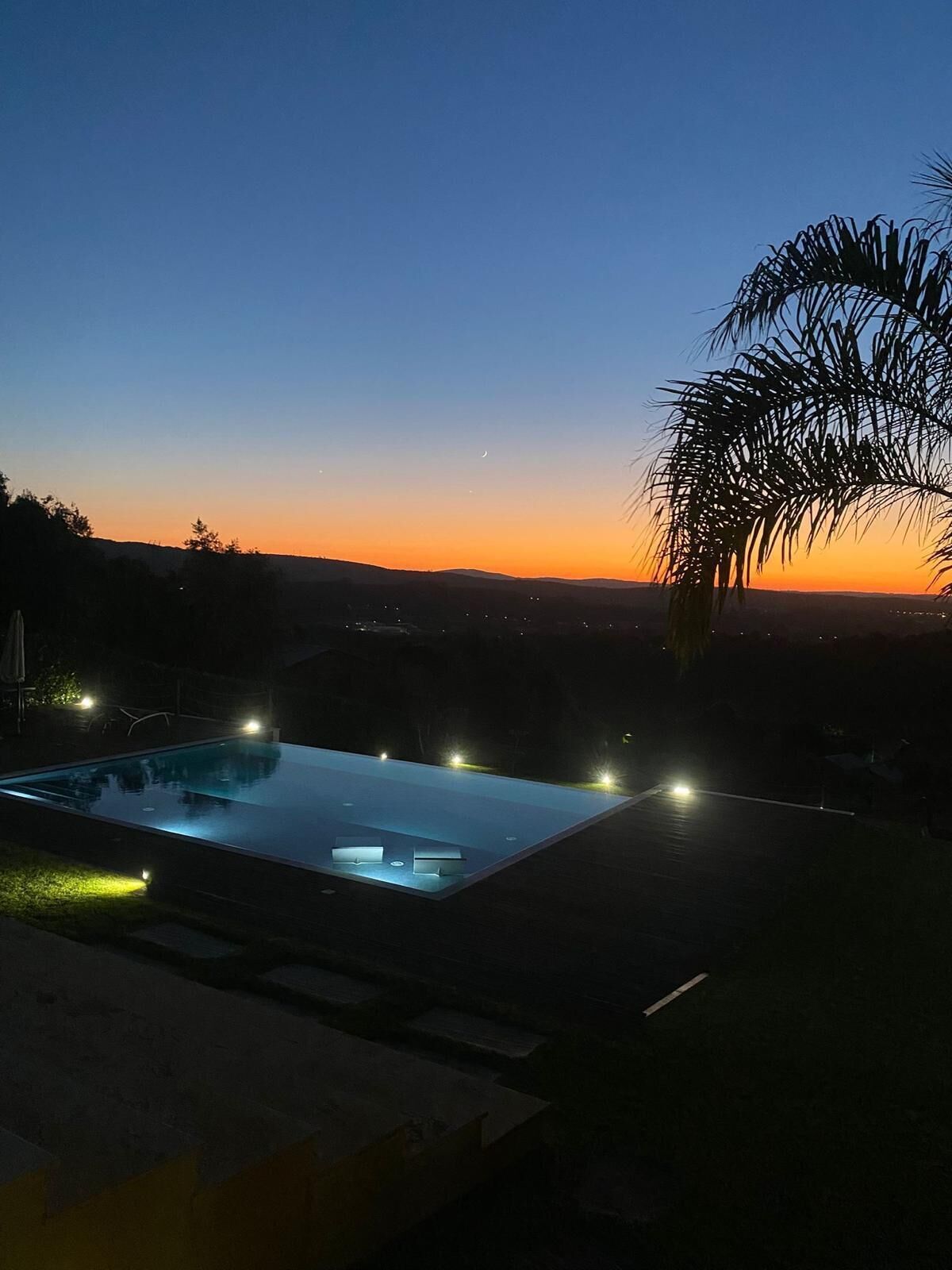 A rectangular swimming pool with a clear view of the surrounding landscape during twilight.