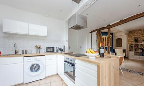 Een moderne keuken met witte kasten, een ingebouwde wasmachine, een houten kookeiland en een stenen muur op de achtergrond.