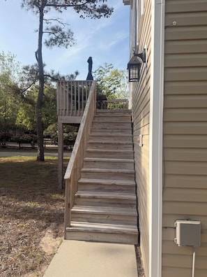 A wooden staircase leading to a deck, surrounded by trees and a house with siding.