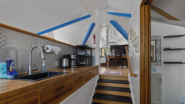 Una cucina moderna con mobili in legno, zoccolo a scacchi bianconero e una scala in legno che conduce a una sala da pranzo.