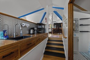 A modern kitchen with wooden cabinets, a black and white checkered backsplash, and a wooden staircase leading to a dining area. - Bright & Colorful Loft Near Hyde Park (Boise)