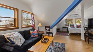 Un soggiorno in stile loft con un divano in pelle nera, un tavolino in legno e un letto con cuscini colorati.