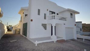 Ein weißes, zweistöckiges Haus mit Balkon, Garage und einem Schotterweg.