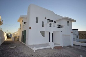 A white two-story house with a balcony, a garage, and a gravel driveway. - Serene oceanview home Vista del Mar (Puerto Peñasco)