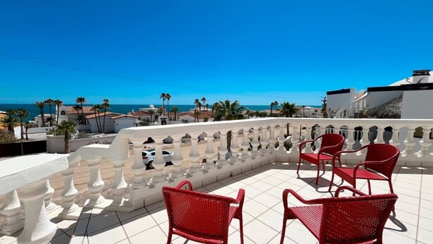 Eine Dachterrasse mit roten Stühlen, weißen Geländern und Blick auf das Meer und Gebäude.