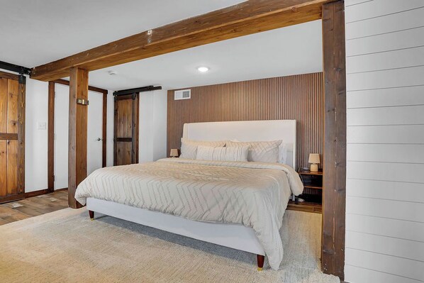 Une chambre à coucher avec un lit, des poutres en bois, un mur à lattes et une tête de lit blanche.