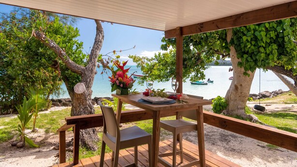 A wooden deck with a table and chairs overlooking a beach with boats and trees. - MATIRA BEACH RAITEA I (Bora Bora)