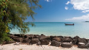 A beach with clear turquoise water, a boat, and large rocks in the foreground. - MATIRA BEACH RAITEA I (Bora Bora)