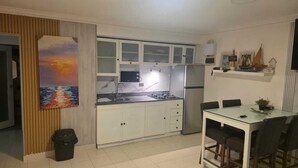 Een kleine keuken met witte kastjes, een roestvrijstalen koelkast, en een eethoek met een glazen tafel en stoelen.