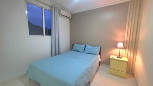 Een slaapkamer met een bed, nachtkastje, lamp en raam.