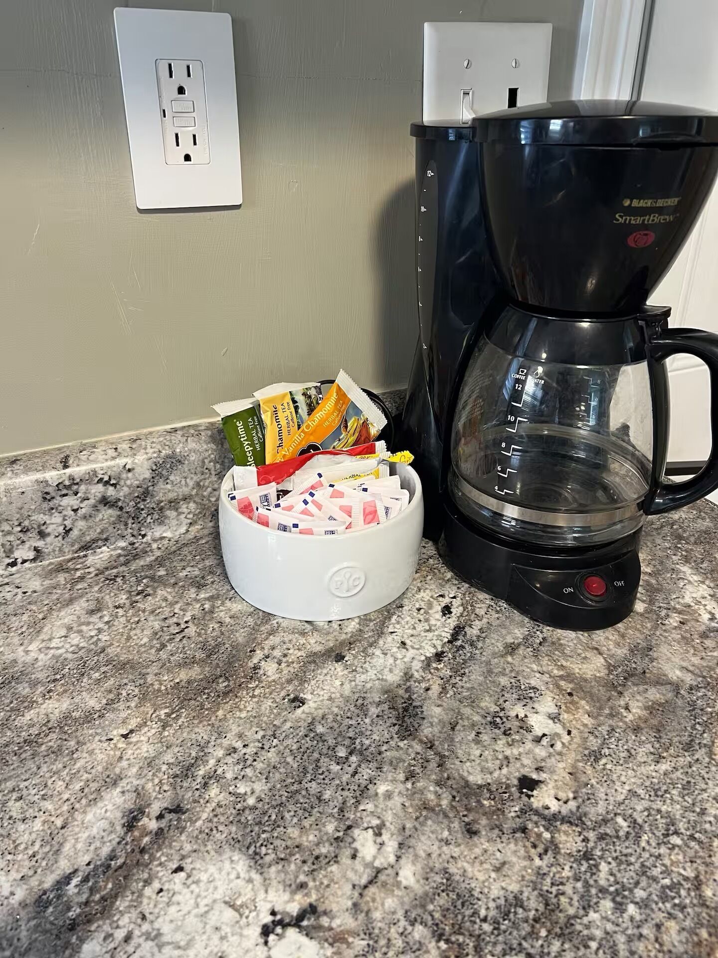 Una cafetera sobre una encimera de granito con un recipiente blanco lleno de cápsulas de café.