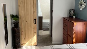 Une chambre à coucher comprenant un lit, une armoire en bois, une commode, un miroir et une porte coulissante donnant sur une salle de bain.