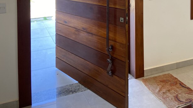 A wooden sliding door with a metal handle, leading to an outdoor area with a view of palm trees and a parked car. - Cozy house. 5 km from BR 040 highway, 10 km from the shopping mall and 15 km from Lagoa Paulino lagoon. (Barreiro de Sete Lagoas)