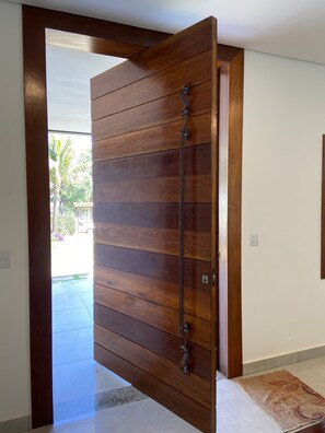 A wooden sliding door with a metal handle, leading to an outdoor area with a view of palm trees and a parked car. - Cozy house. 5 km from BR 040 highway, 10 km from the shopping mall and 15 km from Lagoa Paulino lagoon. (Barreiro de Sete Lagoas)