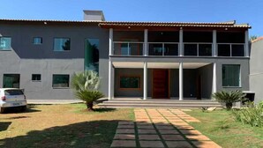 A modern two-story house with a paved driveway, a car parked in the driveway, and a small garden with a palm tree. - Cozy house. 5 km from BR 040 highway, 10 km from the shopping mall and 15 km from Lagoa Paulino lagoon. (Barreiro de Sete Lagoas)