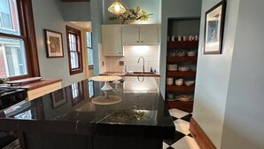 Una cocina con una isla de mármol negro, luces colgantes, un fregadero y suelo de baldosas.