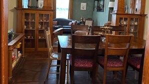 Un comedor con mesa y sillas de madera, ventilador de techo y vista a otra habitación.