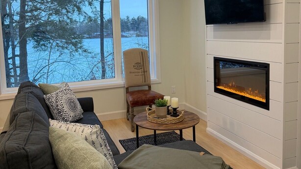 A living room with a sofa, a TV mounted on the wall, and a fireplace. - Cozy waterfront 2-bedroom cottage in peaceful Seeley's Bay with AC (Seeley's Bay)