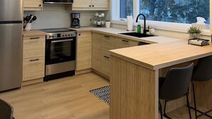 A modern kitchen with wooden cabinets, stainless steel appliances, a large window, and a bar area. - Cozy waterfront 2-bedroom cottage in peaceful Seeley's Bay with AC (Seeley's Bay)