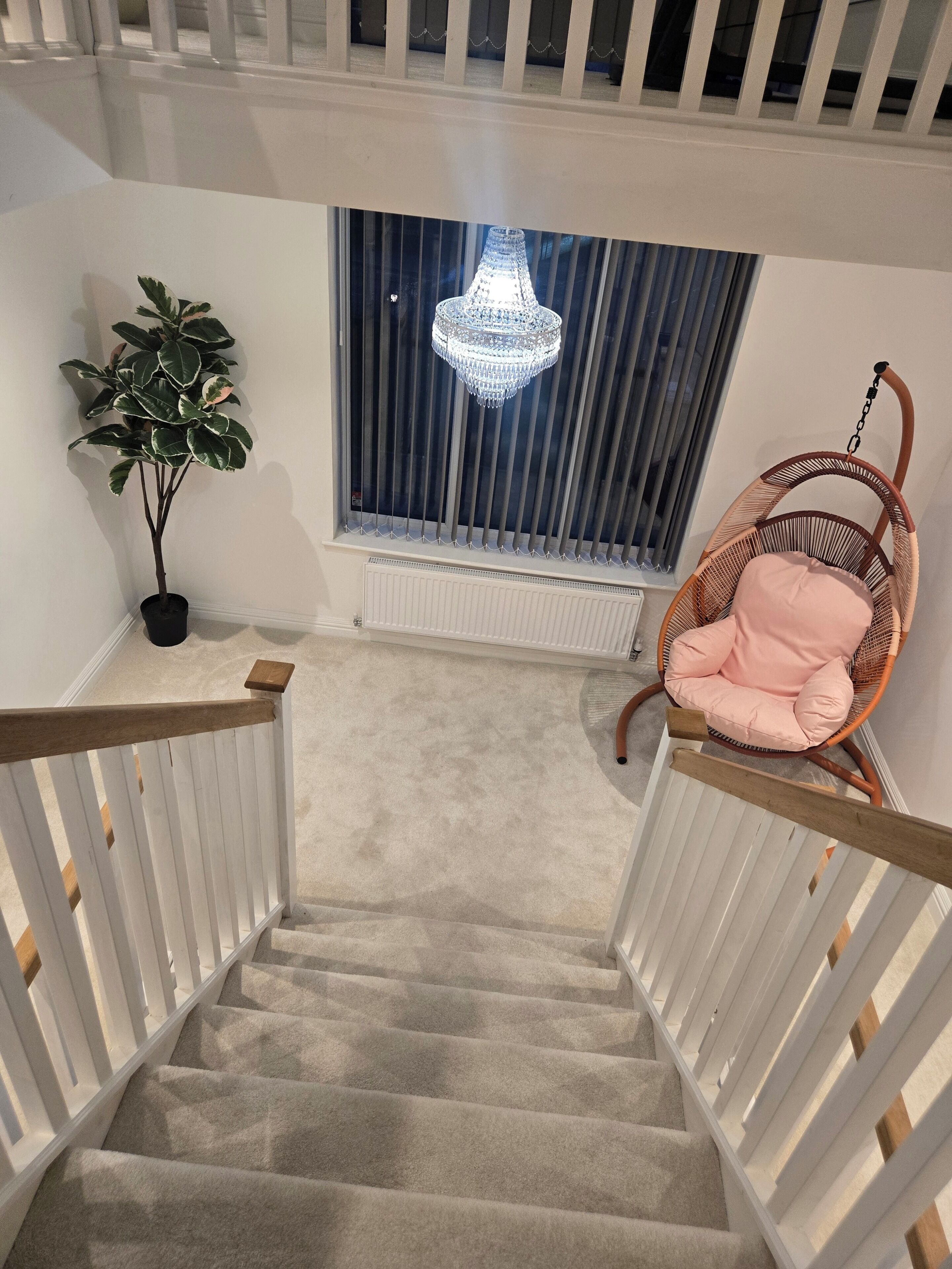 A staircase with a white railing, a hanging chair with a pink cushion, a potted plant, and a chandelier.