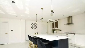 A modern kitchen with a central island, bar stools, pendant lighting, and a clock on the wall. - Glams luxury home (Wolverhampton)