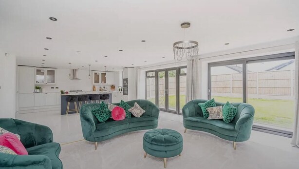 A spacious living area with a green sofa set, a round ottoman, and a large window offering a view of the outdoors. - Glams luxury home (Wolverhampton)