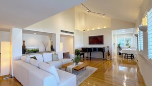 Uma sala de estar ampla com um sofá branco, um piano, uma guitarra e um espaço de jantar com mesa e cadeiras.